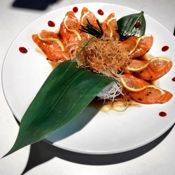 Sakana Sushi Lounge DTLA's salmon sashimi with lemon, chives, crispy garnish, and a banana leaf.