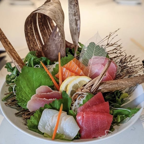 Sakana Sushi Lounge's sashimi platter with tuna, salmon, and white fish, garnished with lemon and greens.